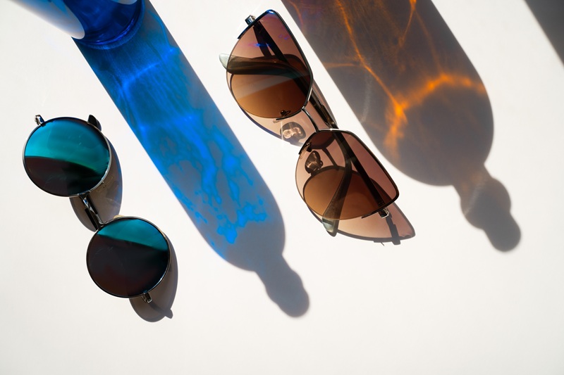 Blue And Brown Sunglasses With Glass Bottle Reflections On White Background. Isolated. Summer Hydration Concept